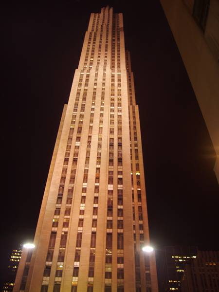 Rockefeller Center skyscraper lit at night, glowing windows in pale stone