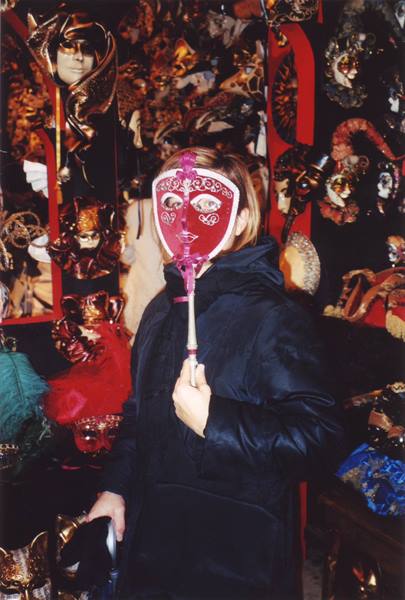 Woman holding red Venetian mask in front of a stall of masks