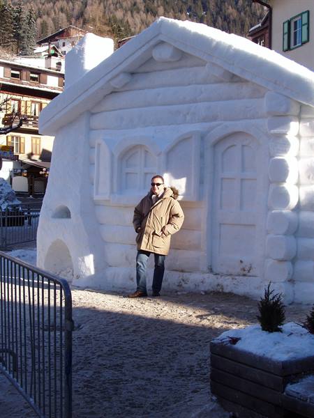 Man in parka posing beside a house sculpted from snow