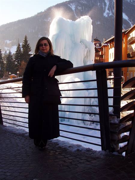 Woman leaning on railing in front of an icy frozen fountain among alpine buildings