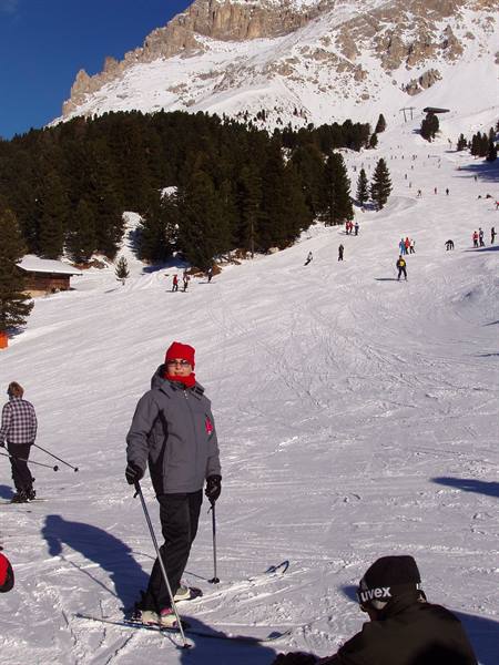 Skier in red hat on snowy slope with fir trees and rocky peaks