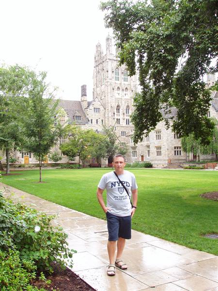 Man in NYPD t-shirt on wet walkway, Princeton University gothic stone buildings behind