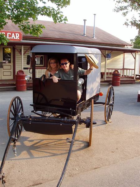 Couple riding a black horse-drawn buggy in front of Country Village shops