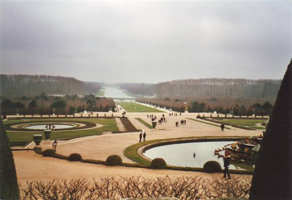 Gardens of Versailles with circular basins and visitors under a grey winter sky