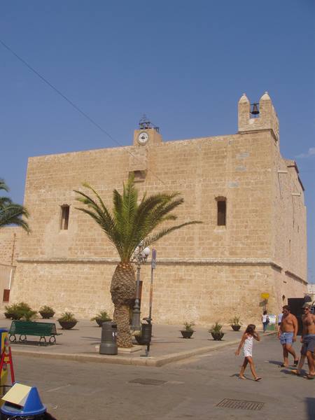 Old stone fortress with bell tower, palm tree and tourists in sunny square