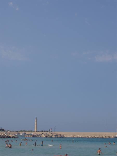 Swimmers in turquoise sea in front of San Vito Lo Capo lighthouse