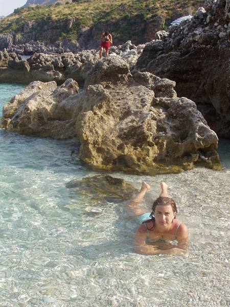 Woman lying in shallow clear water near limestone rocks, man in red above