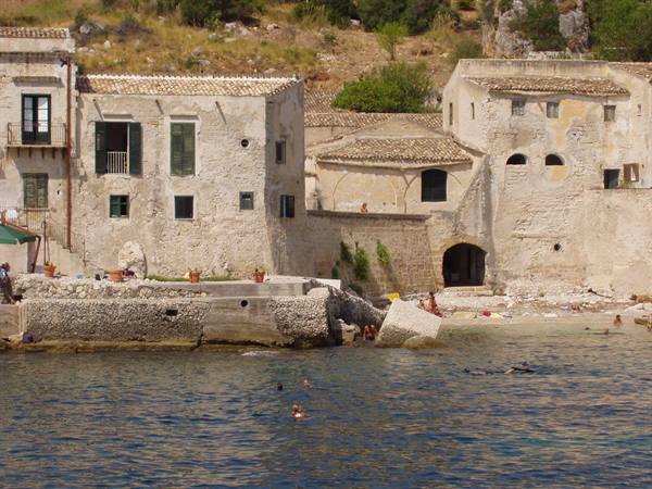 Swimmers in front of the old stone buildings of Tonnara di Scopello