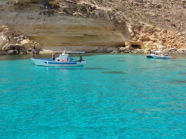 White boats anchored on turquoise water in front of limestone cliffs