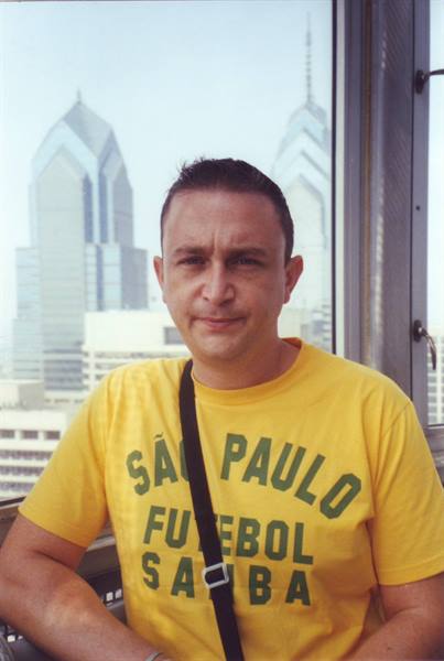 Man in yellow São Paulo Futebol Samba shirt with skyscrapers behind a window