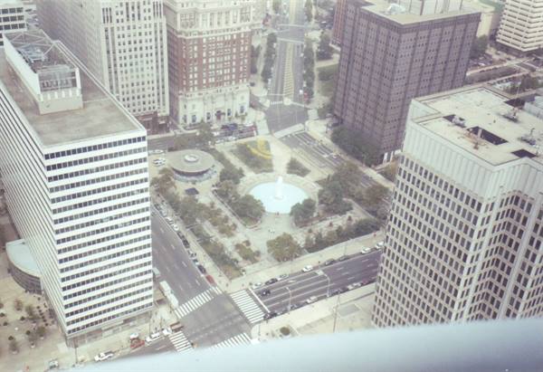 Skyscrapers around a plaza with central fountain, streets with cars, daylight