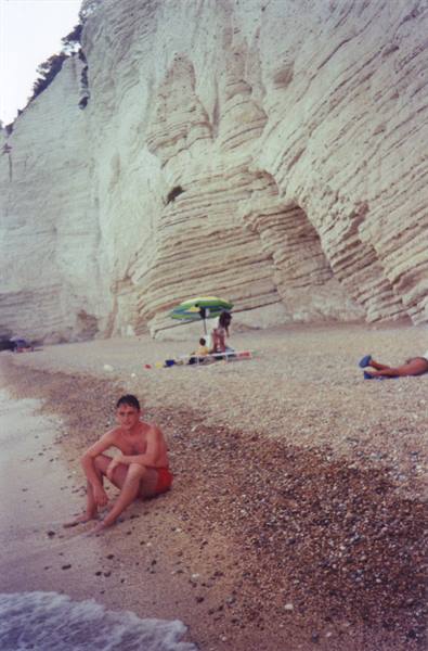 Boy sitting on pebble beach beneath white chalk cliffs, beach umbrella
