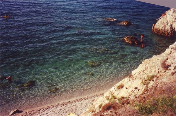 Swimmers on white rocks and clear water with rocky seabed