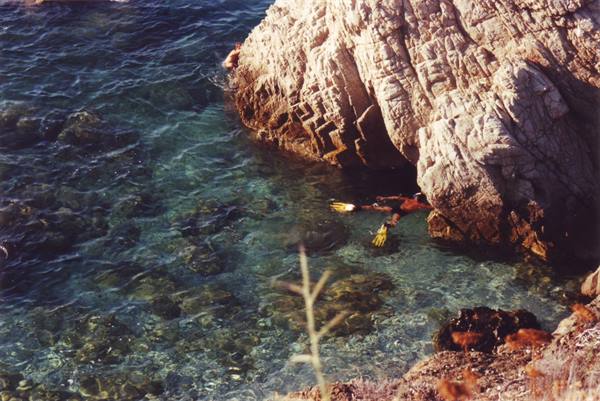 Snorkeler with yellow fins beside a rock formation, clear green water