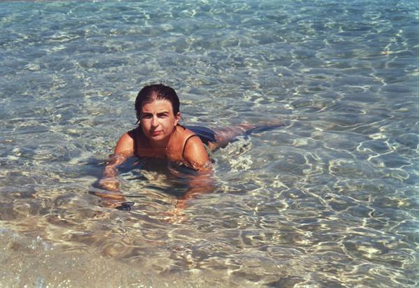 Woman in black swimsuit swims in clear sunlit shallow water