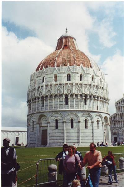 Tourists walk in front of the white marble Baptistery of Pisa