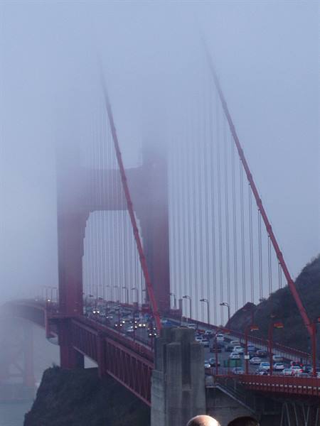 Golden Gate Bridge shrouded in fog, heavy traffic on the roadway