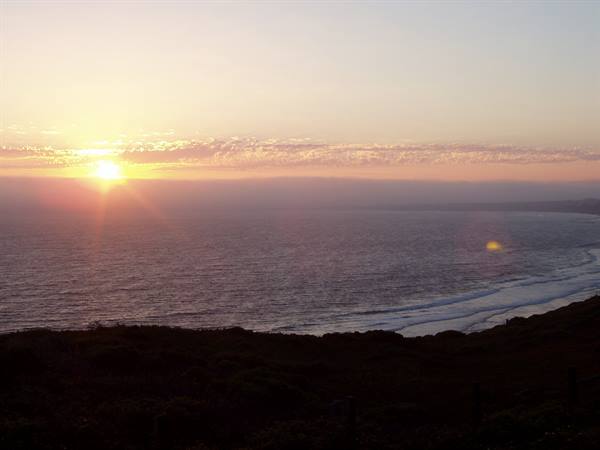 The low sun lights the ocean as waves break on the dark shore