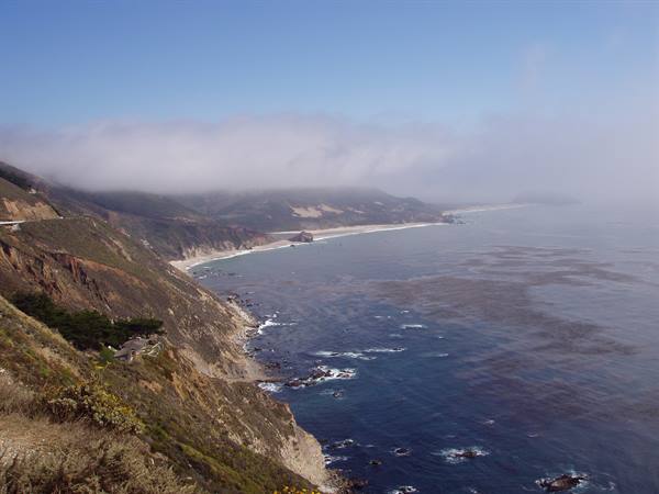 Rocky Big Sur coastline with low fog over the ocean and roads along hills