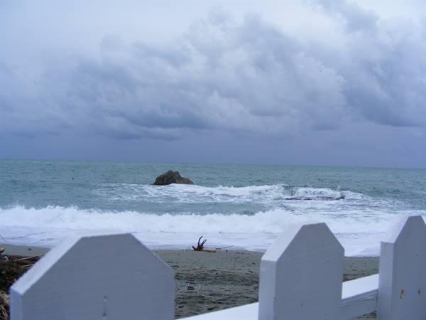 Waves on the beach under dark clouds, white wooden fence in foreground