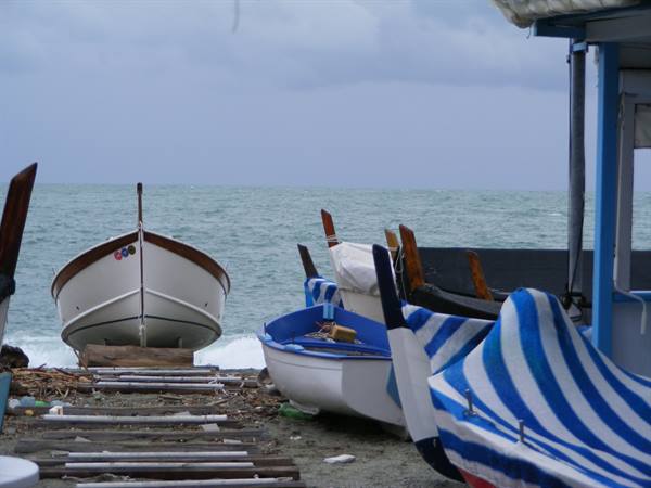 Wooden boats with blue tarps on the beach, rough sea and gray sky