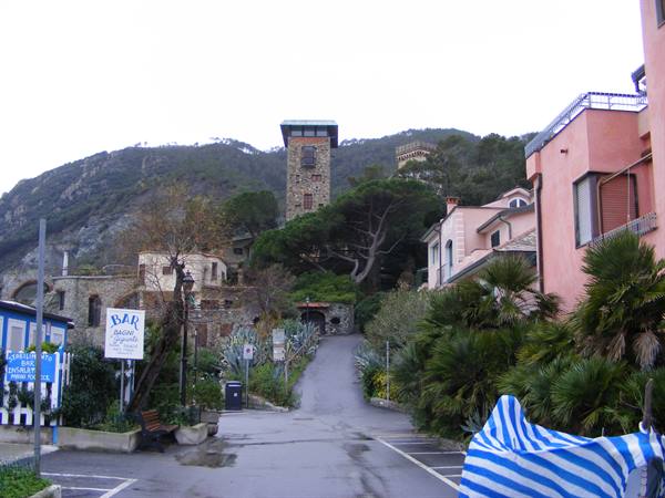 Uphill road with stone tower among green hills and palms in Monterosso