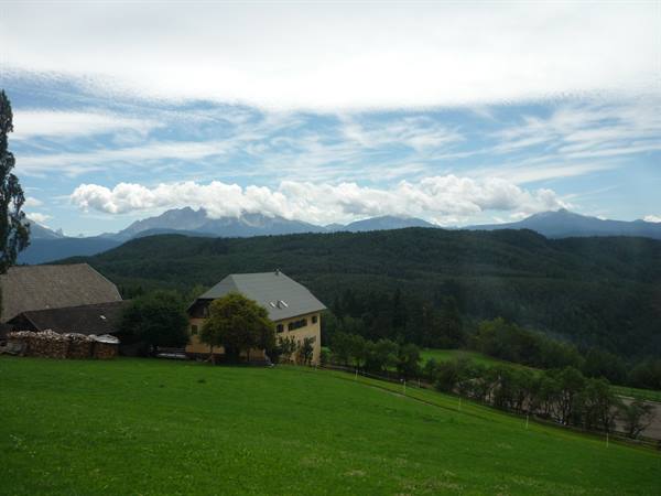 Wooden-roofed farmhouse on green meadow, cloudy mountains behind