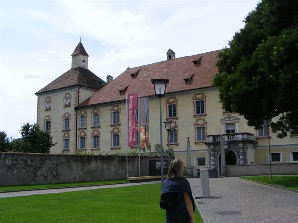 Woman walks toward the baroque Bressanone palace with red roof and banner