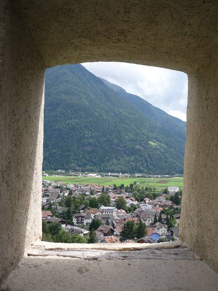 Alpine village among green fields framed by a stone castle window