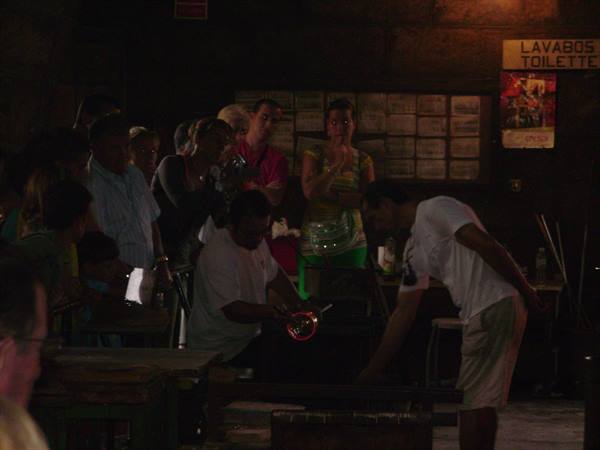 Visitors watch an artisan shaping glowing glass near the furnace