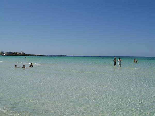 Bathers in clear turquoise water, white sandy beach and clear sky