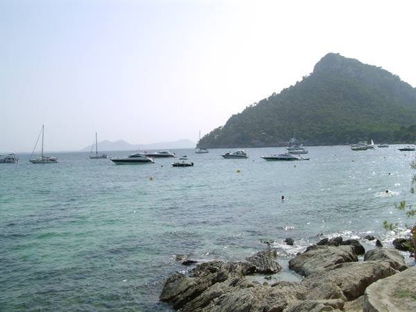 Boats anchored in a turquoise bay with rocks and green hill, Formentor