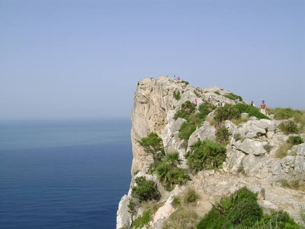 Tourists walk along the limestone rock of Cap de Formentor above the blue sea
