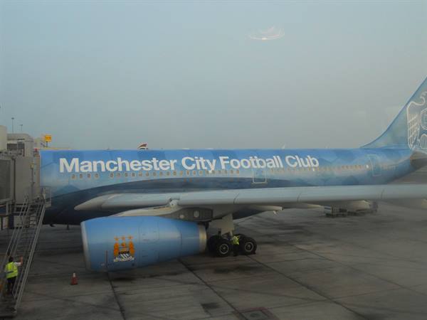 Manchester City Football Club blue plane parked on tarmac with ground crew