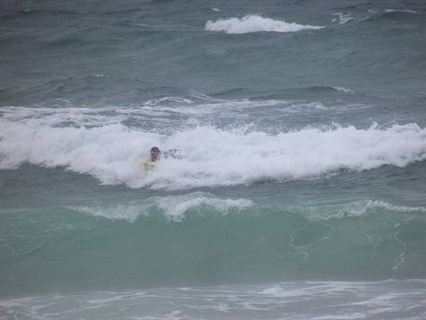 Surfer in wetsuit on yellow board among foamy green waves