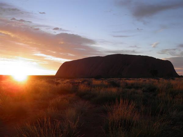 Sunrise behind Uluru, sandstone monolith rising above Australian desert scrub