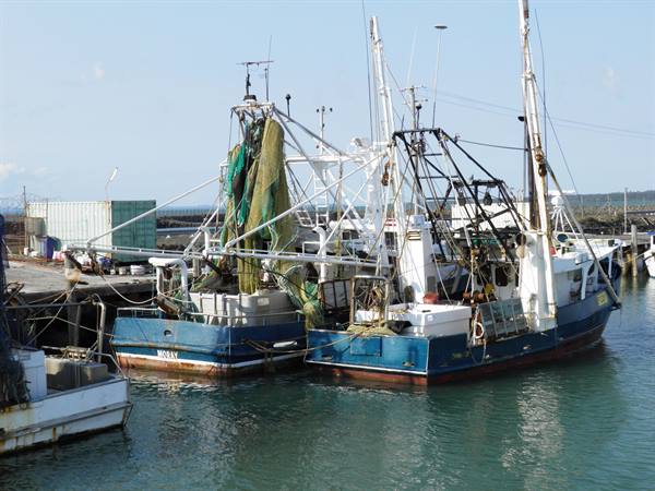 Blue fishing boats moored at the harbor with trawling nets and gear