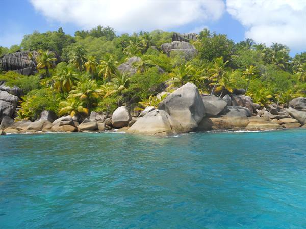 Granite boulders among palms and tropical vegetation on turquoise sea, Seychelles