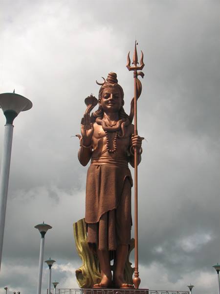 Bronze Shiva statue holding a trident, against a cloudy sky