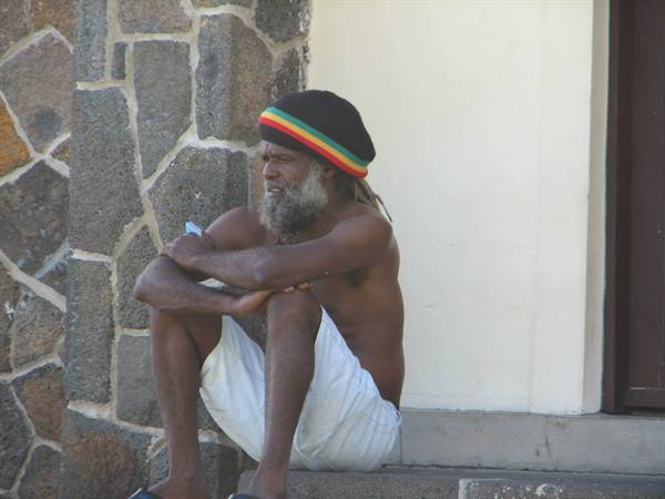 Shirtless rasta man in wool hat sitting on stone steps