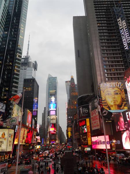 Times Square under grey sky, glowing billboards and crowds among skyscrapers