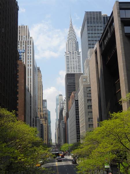 The Chrysler Building towers over a tree-lined street with traffic in New York
