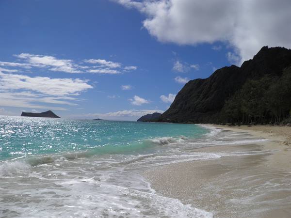 Foamy wave on pale sand at Waimanalo, green mountains and cloudy sky