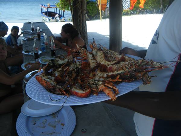 Waiter serving plate of grilled lobsters at beachside stall