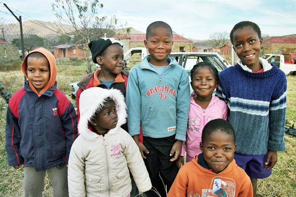 Group of smiling children in front of rural houses and a car
