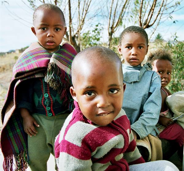 African children gaze at the camera, wrapped in sweaters and colorful blankets under bare trees