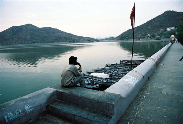 Man sitting on stone embankment beside moored boats, Fateh Sagar lake, Udaipur