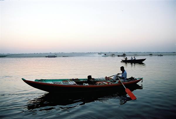 Boatman rows a long wooden boat on the Ganges in Varanasi, misty dawn