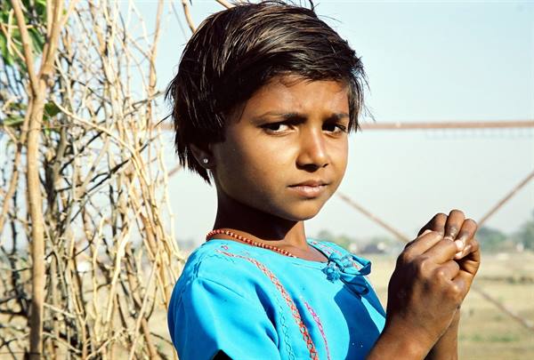 Girl in blue shirt with red necklace among dry branches