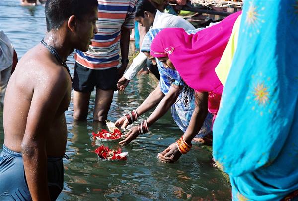 Women in pink saris offer red flowers to the Ganges river, Varanasi